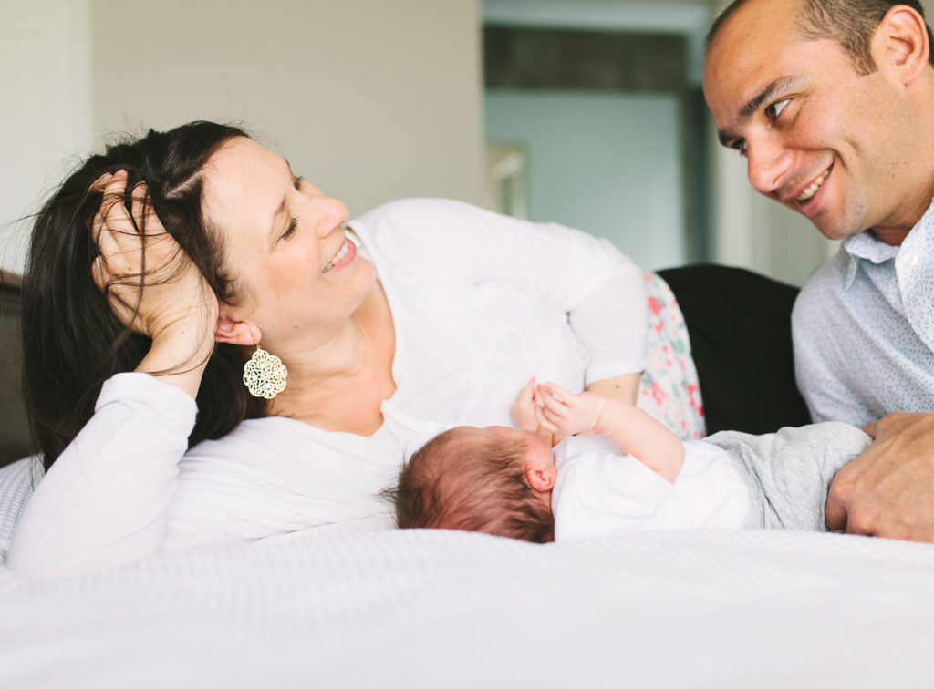 parents laying on bed with newborn baby